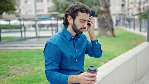 パークでコーヒーを飲むスマートフォンで音声メッセージを聞く若いヒスパニック男性 — ストック動画