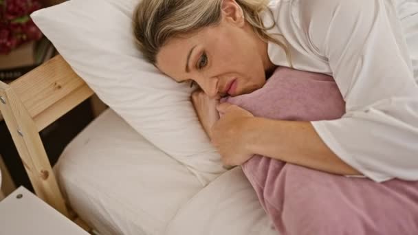 寝室で泣いている悲しい表情でベッドに横たわる若い金髪の女性 — ストック動画