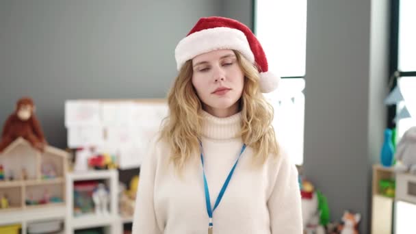 幼稚園に立っているクリスマスの帽子をかぶっている若い金髪の女性プリスクール教師 — ストック動画
