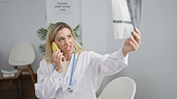 若い金髪の女性医師は診療所の待合室でスマートフォンで話しているX線を見ています — ストック動画