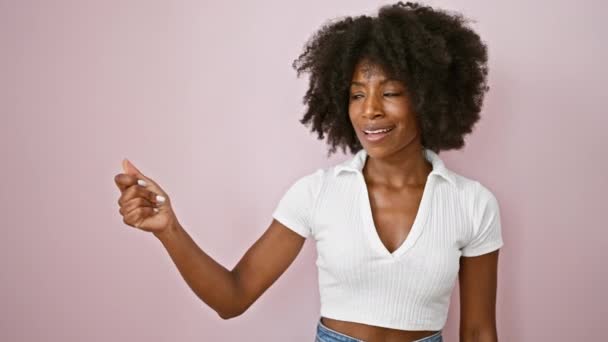 アフリカ系アメリカ人の女性がピンクの背景の向こうを指差して笑っている — ストック動画