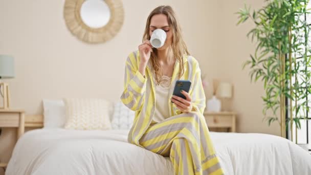 Young Blonde Woman Using Smartphone Drinking Coffee Bedroom — Stockvideo
