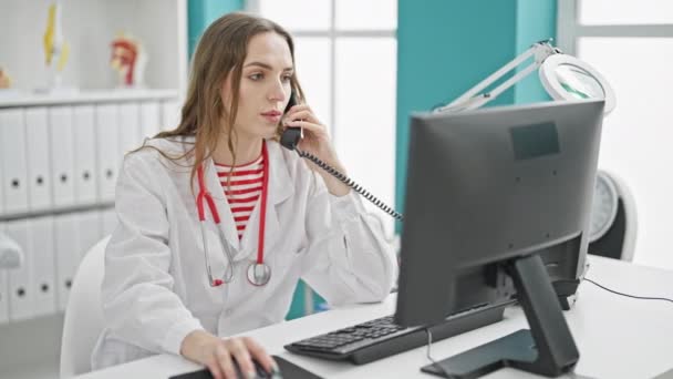 Młoda Blondynka Lekarz Pomocą Komputera Rozmawia Przez Telefon Klinice — Wideo stockowe