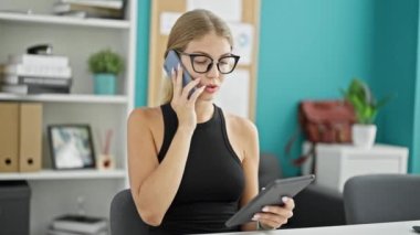Genç sarışın iş kadını dokunmatik ped kullanıyor. Ofiste akıllı telefondan konuşuyor.