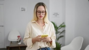 Genç sarışın iş kadını ofiste akıllı telefon kullanıyor.