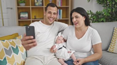 Üç kişilik aile evdeki kanepede selfie çekiyor.