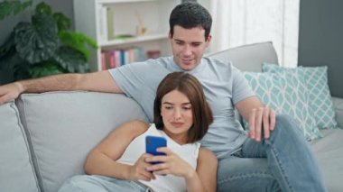 Kanepede birlikte oturan güzel çift evde akıllı telefon beşliği kullanıyor.