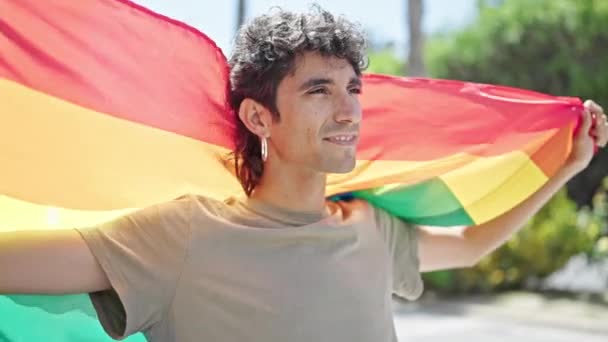 若いヒスパニックの男は 路上で虹の旗を着て自信を持って微笑みます — ストック動画