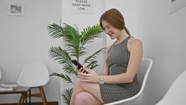 年轻的金发女子坐在椅子上 用智能手机在候车室庆祝 — 图库视频影像