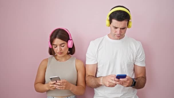 美丽的一对情侣 用智能手机和耳机站在孤立的粉色背景上 — 图库视频影像