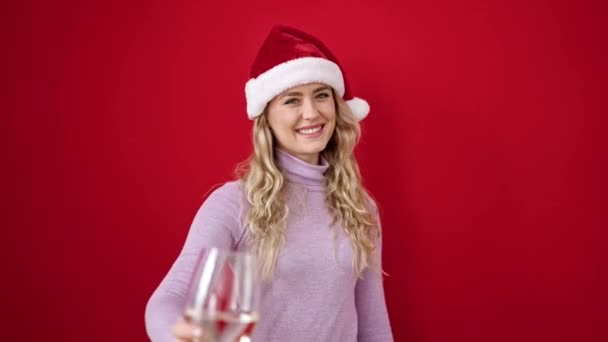 Młoda Blondynka Nosi Świąteczny Kapelusz Trzymając Kieliszek Wina Odizolowanym Czerwonym — Wideo stockowe