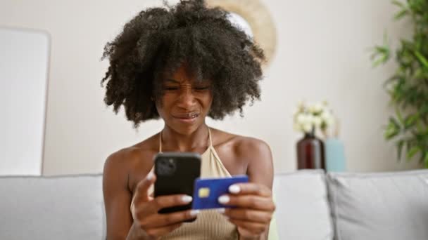 拿着智能手机和信用卡购物的非洲裔美国女人在家里看起来很沮丧 — 图库视频影像