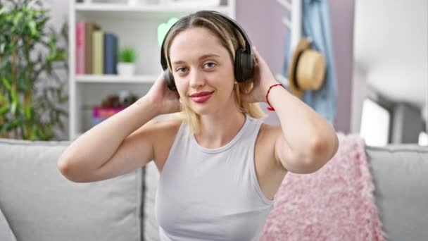 Młoda Blondynka Słuchająca Muzyki Siedząca Kanapie Uśmiechnięta Domu — Wideo stockowe