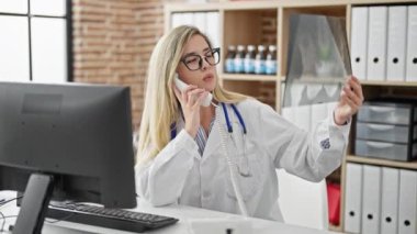 Young blonde woman doctor talking on telephone holding xray at clinic