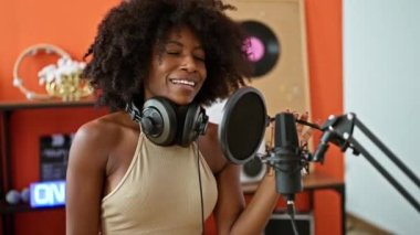 Müzik stüdyosunda şarkı söyleyen kulaklık takan Afrikalı Amerikalı kadın müzisyen.