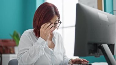 Ofiste çalışan orta yaşlı bir iş kadını gözlüğünü çıkartıyor.