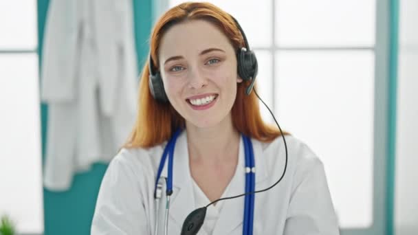 若い赤毛の女性の医者は診療所のヘッドセットが付いているビデオ通話をする — ストック動画