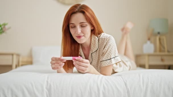Νεαρή Κοκκινομάλλα Γυναίκα Χαμογελά Αυτοπεποίθηση Κρατώντας Τεστ Εγκυμοσύνης Στο Υπνοδωμάτιο — Αρχείο Βίντεο
