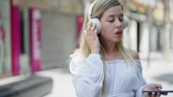 Νεαρή Ξανθιά Γυναίκα Χρησιμοποιώντας Smartphone Και Ακουστικά Που Έχουν Δωρεάν — Αρχείο Βίντεο