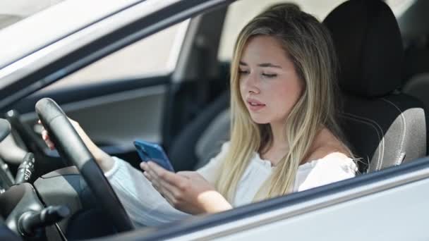 若い金髪の女性は 路上に車に座っているスマートフォンを使用して — ストック動画