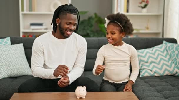 Африканский Американец Отец Дочь Вставляют Монету Копилку Сидя Дома Диване — стоковое видео