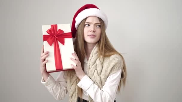 Молодая Блондинка Рождественской Шляпе Слушает Подарочный Звук Изолированном Белом Фоне — стоковое видео