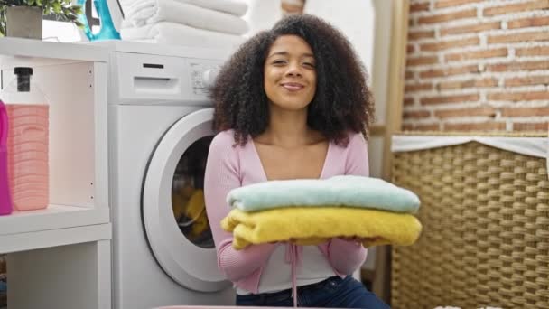 アフリカ系アメリカ人女性 洗濯室で折り畳まれたタオルを持っている服を洗濯 — ストック動画