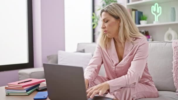 若い金髪の女性は 自宅でクッションで顔を覆うソファに横たわって深刻な顔でノートパソコンを閉じる — ストック動画