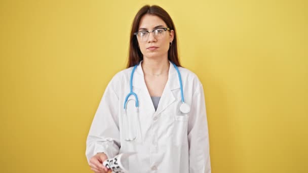 若い美しいヒスパニックの女性医師は深刻な表現で立っている私たちはあなたが単離された黄色の背景の上に紙を必要とします — ストック動画
