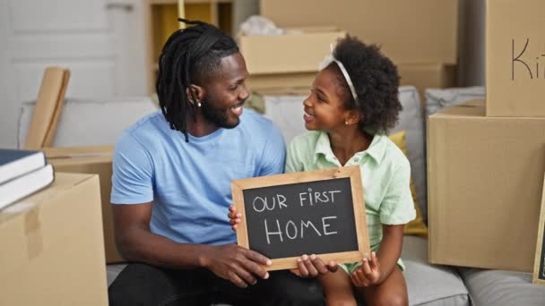 アフリカ系アメリカ人の父親と娘は 新しい家でソファーに座って黒板を持っています — ストック動画
