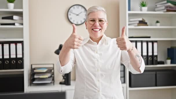 中年の灰色の髪の女性のビジネスワーカーは オフィスで親指のジェスチャーをする自信を持って微笑みます — ストック動画