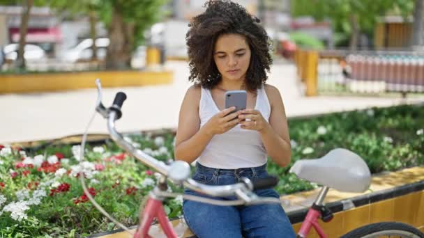 Junge Schöne Hispanische Radfahrerin Sitzt Mit Smartphone Auf Parkbank — Stockvideo