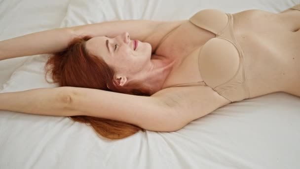 年轻的红头发女人穿着内衣躺在床上笑着躺在卧室里 — 图库视频影像