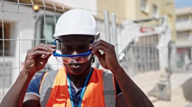 İnşaat alanında gözlük takarak gülümseyen Afrikalı Amerikalı bir inşaatçı.