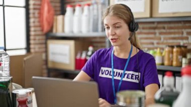Genç sarışın kadın gönüllü olarak yardım merkezinde masada oturmuş gülümsüyor.