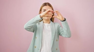 Genç sarışın iş kadını, kendine güvenen, izole pembe arka planda kalp hareketi yapan, gülümseyen.