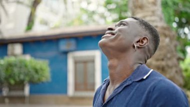 Afro-Amerikalı adam parkta kendine güvenerek gülümsüyor.