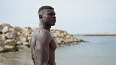 Afrika kökenli Amerikalı turist plajda ciddi yüzüyle üstsüz duruyor.