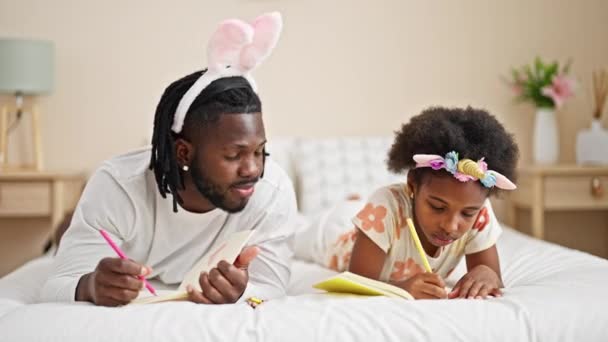 アフリカ系アメリカ人の父親と娘は寝室のベッドに横たわるノートブックに面白い日記を着ています — ストック動画