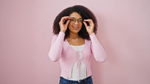 アフリカ系アメリカ人女性は 孤立したピンクの背景の上にメガネを取る自信を持って微笑みます — ストック動画