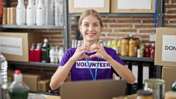 若い金髪の女性ボランティアは チャリティセンターでハートジェスチャーをしているノートパソコンを使用して — ストック動画