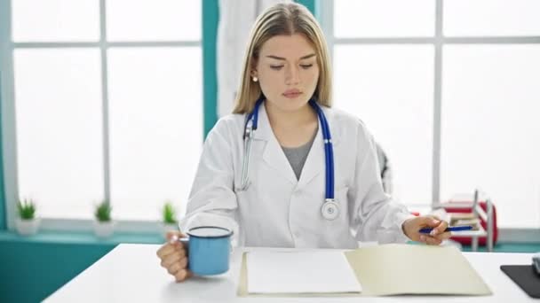 年轻的金发女医生喝咖啡 在诊所写医疗报告 — 图库视频影像