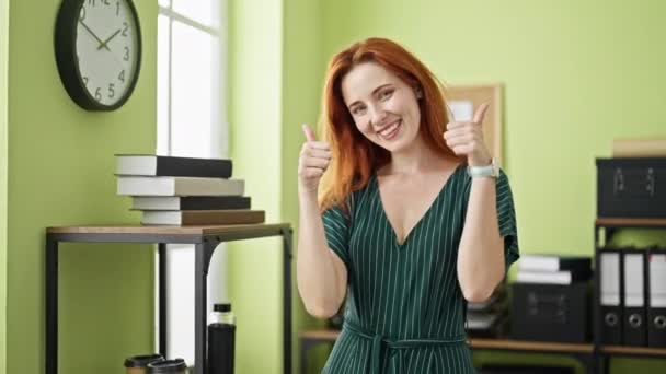 年轻的红头发女商人微笑着自信地在办公室做着竖起大拇指的手势 — 图库视频影像