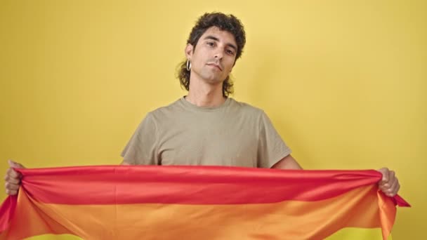 在孤立的黄色背景下 年轻而惊慌的男子举着彩虹旗 表情轻松自在 — 图库视频影像