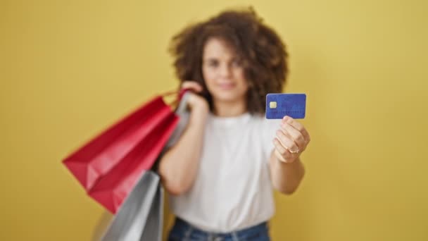 ショッピングバッグとクレジットカードを保持している若い美しいヒスパニックの女性は 孤立した黄色の背景に微笑みます — ストック動画