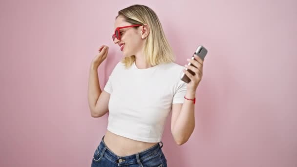 Młoda Blondynka Tańczy Słuchając Muzyki Smartfonie Odizolowanym Różowym Tle — Wideo stockowe