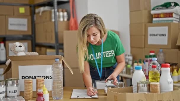 Joven Mujer Rubia Voluntaria Escribiendo Productos Verificación Documentos Centro Caridad — Vídeo de stock