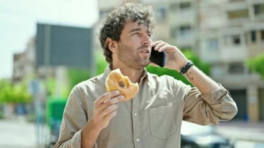Genç İspanyol adam donut yiyor ve akıllı telefondan konuşuyor.