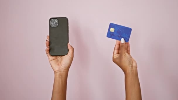 持有智能手机和信用卡的非洲裔美国女性 背景为孤立的粉色 — 图库视频影像