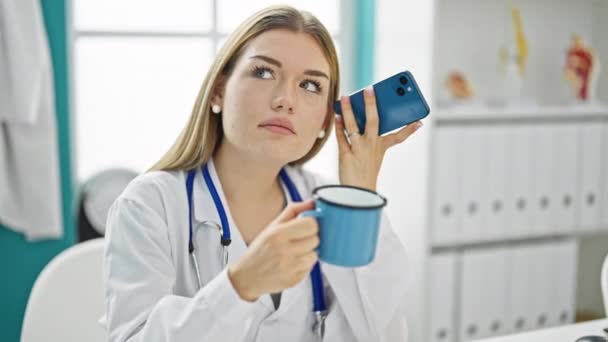 年轻的金发女医生在诊所用智能手机听留言 — 图库视频影像
